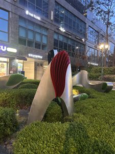 A modern abstract sculpture made of metal with curved and flowing shapes, featuring bright red and green elements. 