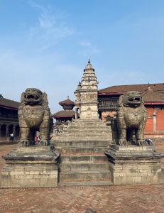 Ancient stone temple steps flanked by two large stone lion statues, leading up to a traditional temple pagoda with intricate carvings, set against a clear blue sky at Bhaktapur Durbar Square.