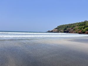 A tranquil beach scene featuring gentle waves lapping at the shore, with a clear blue sky overhead.