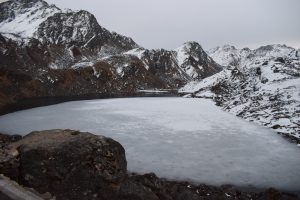 A serene landscape featuring a partially frozen lake surrounded by rugged mountains.