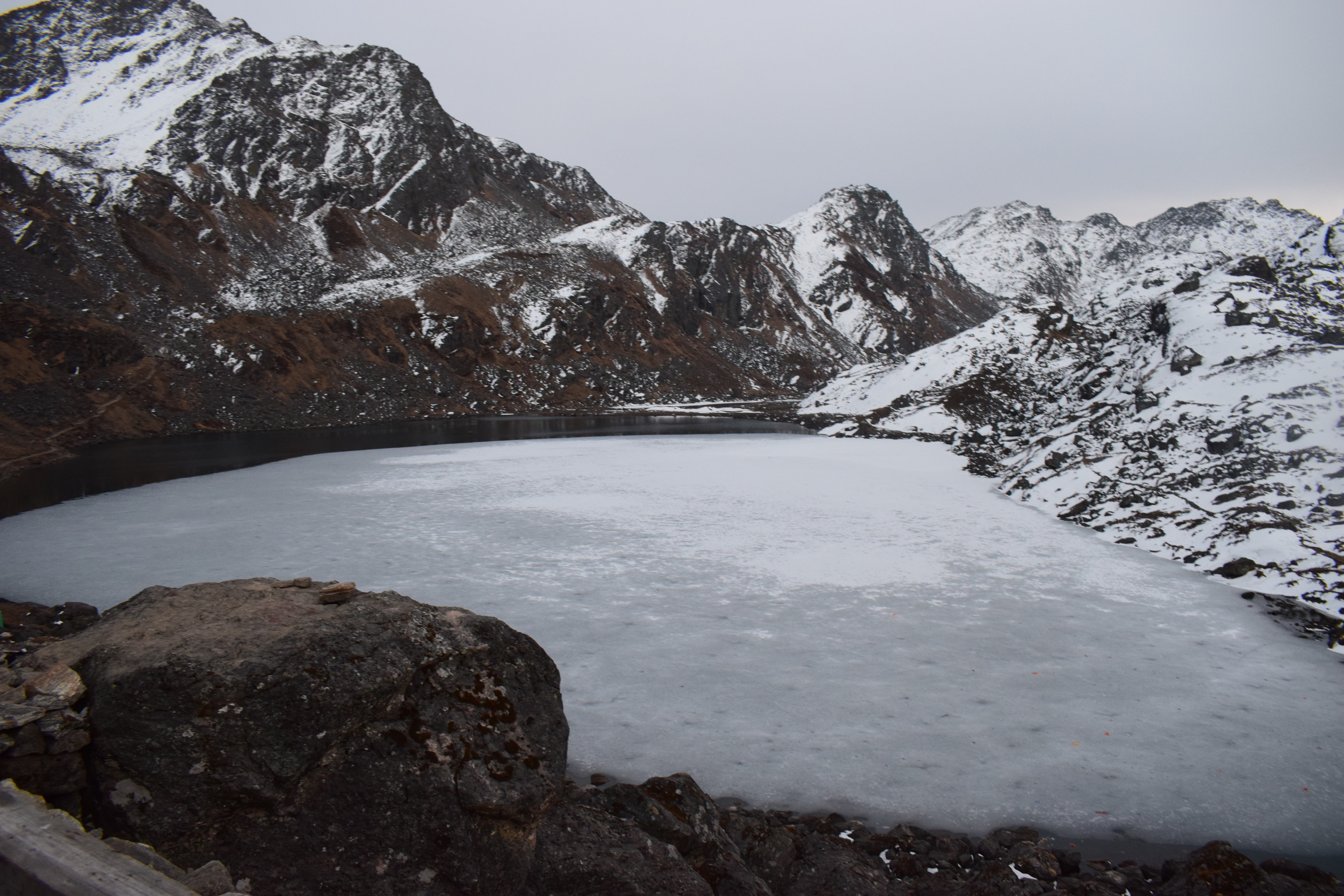 A serene landscape featuring a partially frozen lake surrounded by rugged mountains.