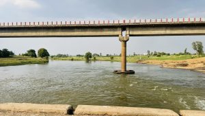 A concrete bridge over a flowing river with grassy banks and a cloudy sky.