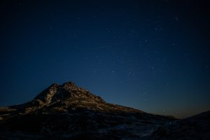 A mountain under a clear, starry night sky, with numerous stars visible above the dark silhouette of the rocky peak.