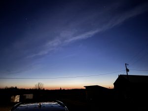 Even sky over a farm. Noctilucent clouds visible. Constellations Taurus the bull and the Pleiades visible in the sky. 
