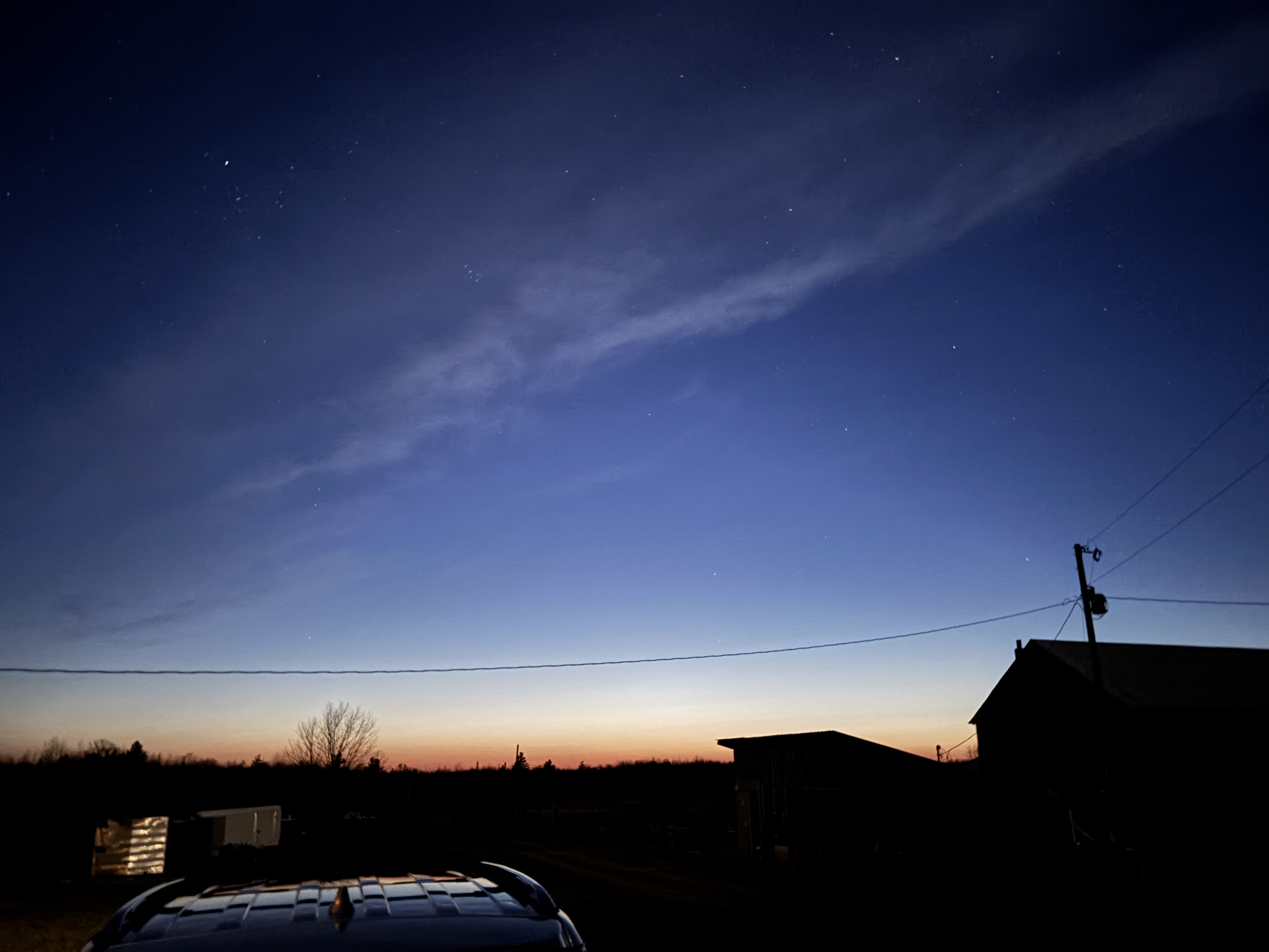 Even sky over a farm. Noctilucent clouds visible. Constellations Taurus the bull and the Pleiades visible in the sky.