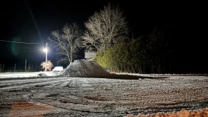 A snow covered yard, with all the snow piled in the middle.  A night scene.