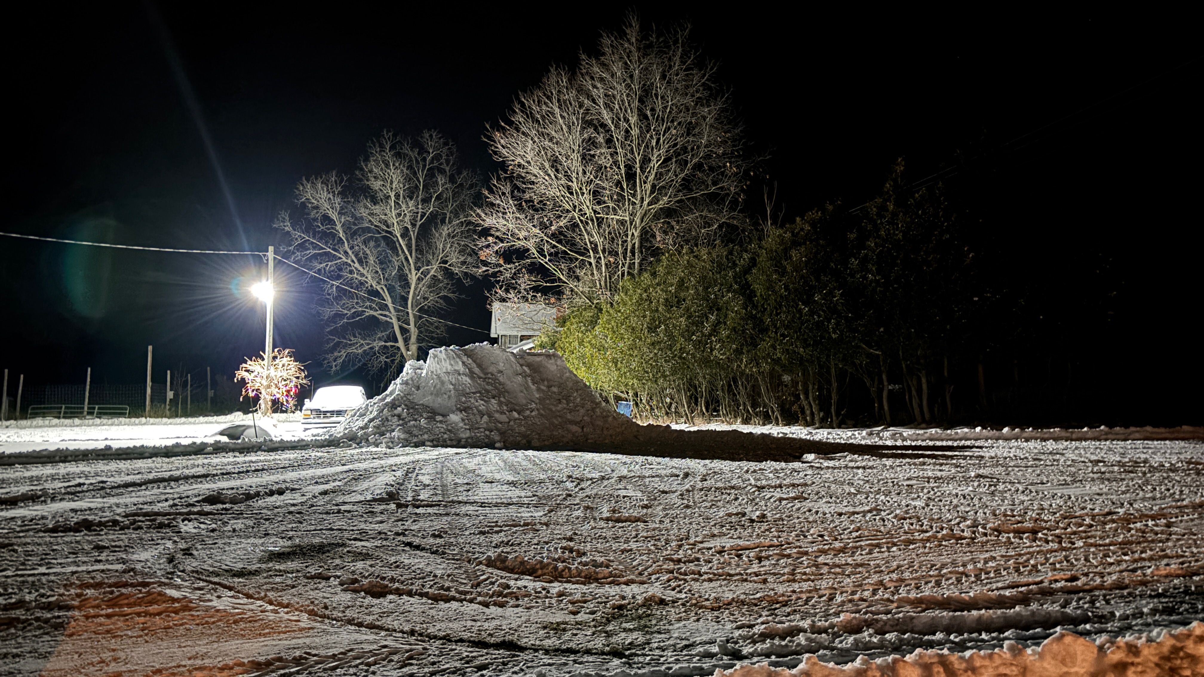 A snow covered yard, with all the snow piled in the middle. A night scene.
