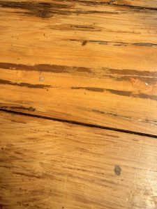Close-up view of a wooden surface with visible grains and some dark streaks and marks, showing natural textures and imperfections