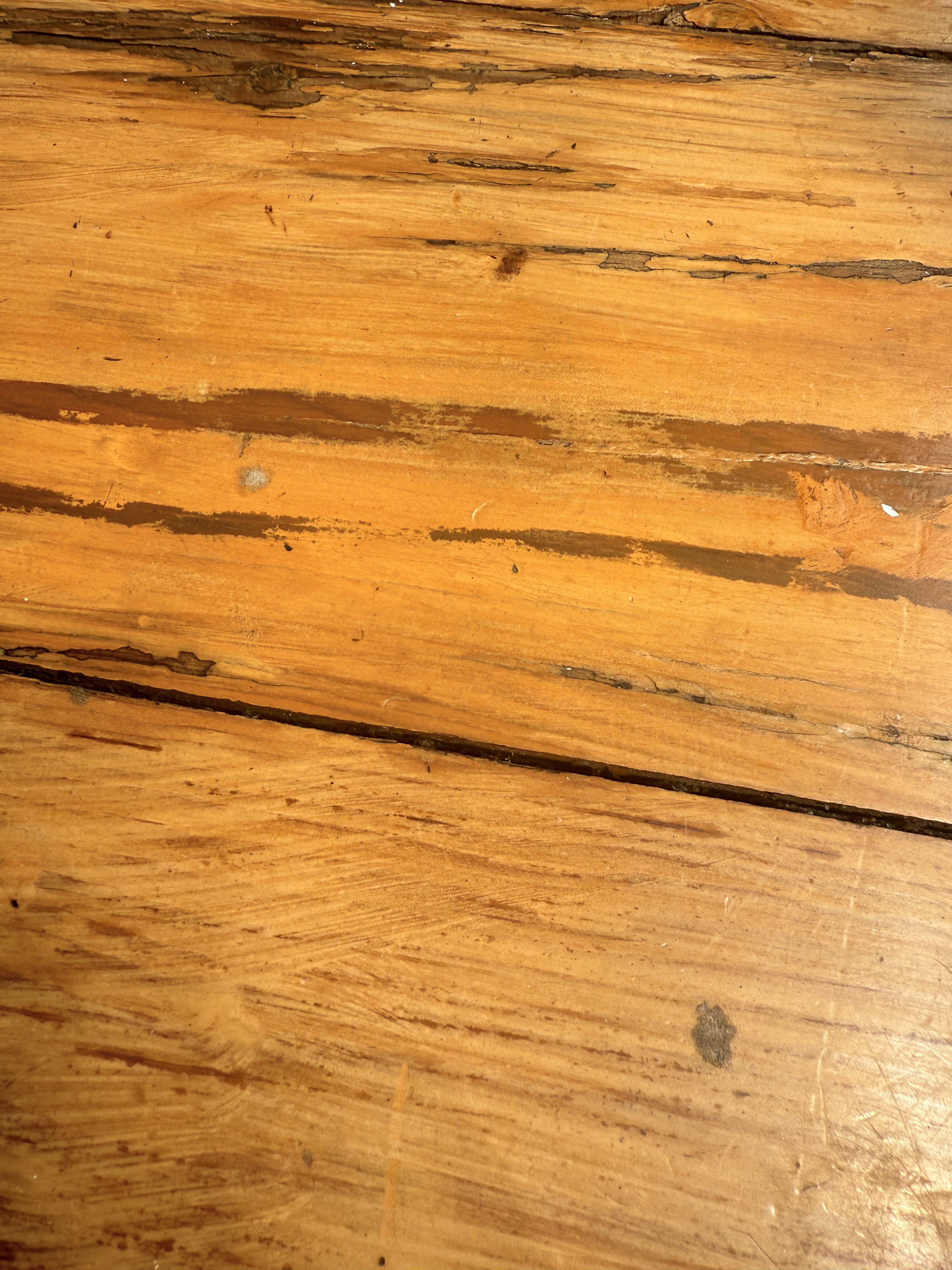 Close-up view of a wooden surface with visible grains and some dark streaks and marks, showing natural textures and imperfections