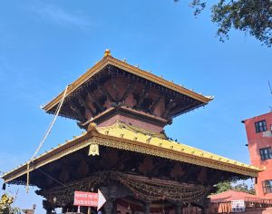 

A traditional multi-tiered pagoda-style Manakamana temple with a golden roof and ornate carvings, set against a clear blue sky.