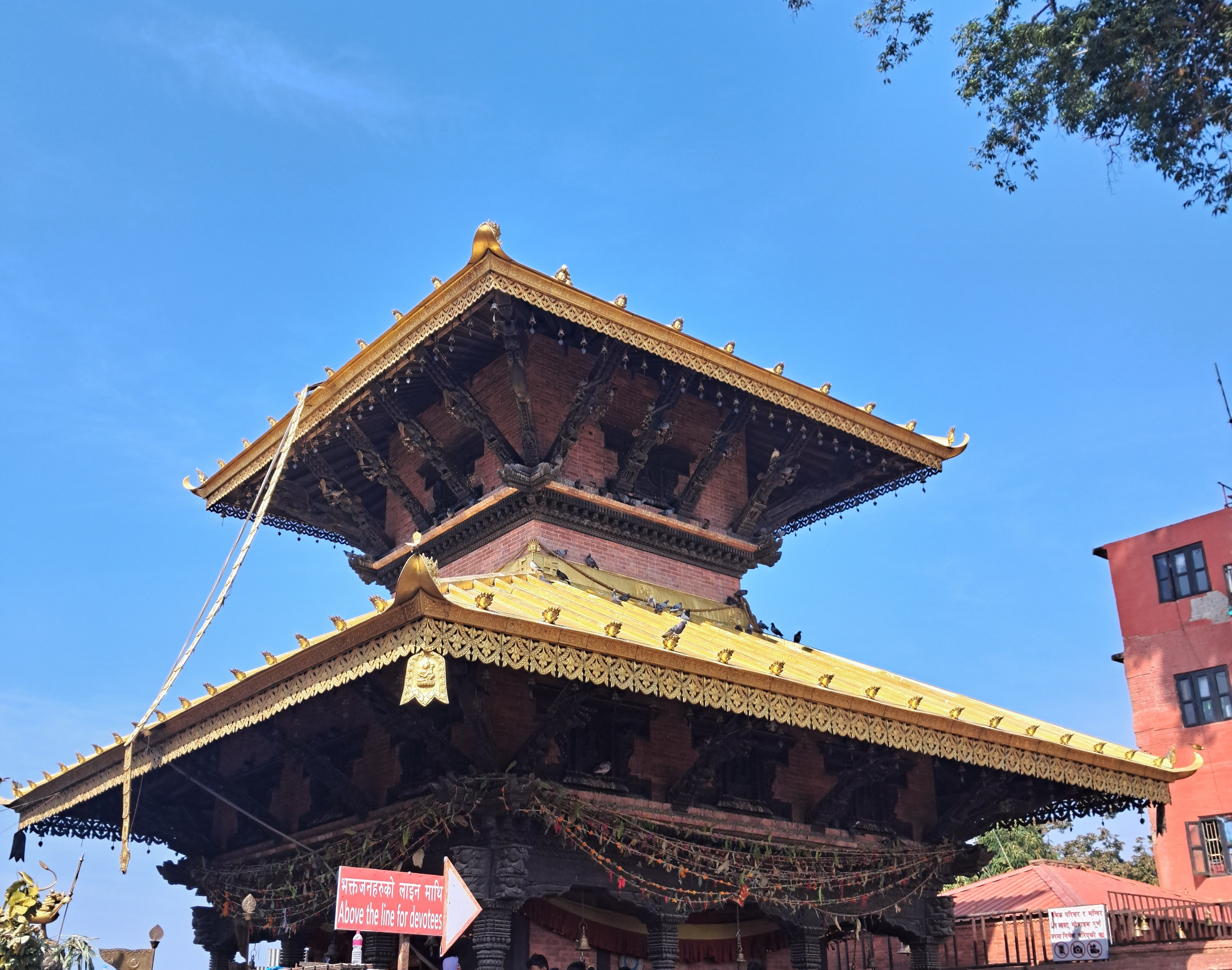 A traditional multi-tiered pagoda-style Manakamana temple with a golden roof and ornate carvings, set against a clear blue sky.