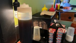 Condiments on a restaurant table, syrup, salt and pepper, mustard and catsup, jam, jelly, and paper napkins.
