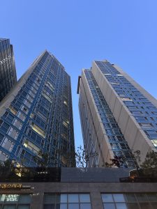A low-angle view of two tall, modern skyscrapers reaching towards a clear blue sky.
