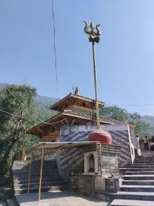 A stone temple with a multi-tiered wooden roof, surrounded by trees, set against a clear blue sky