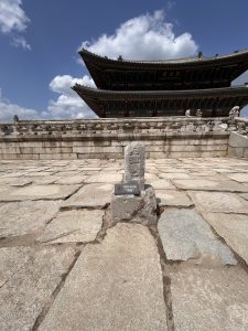 The image shows a traditional Korean building with a distinctive curved roof, partially obscured by clouds in the background.