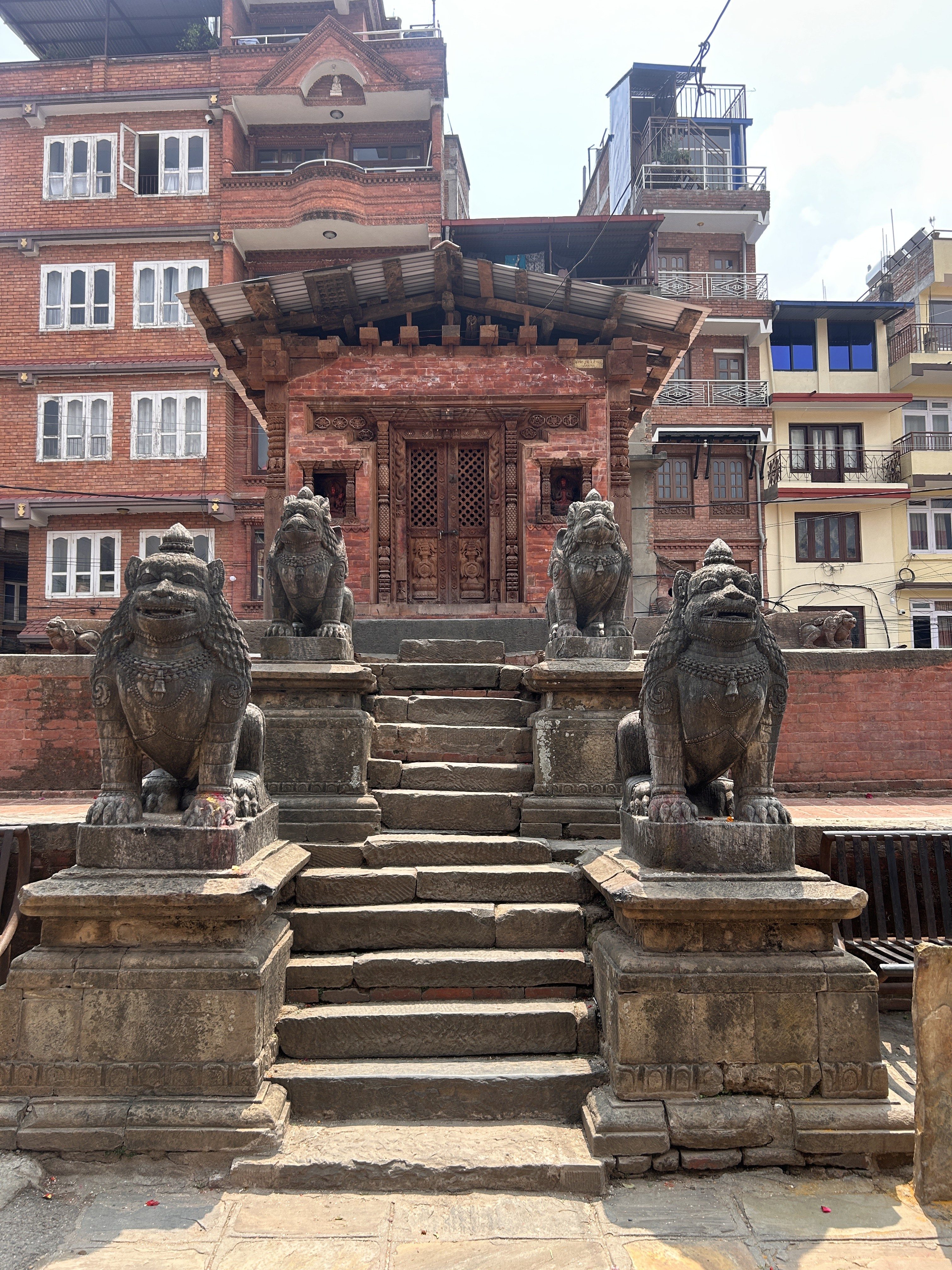 Stone steps leading up to a traditional brick building, flanked by four stone lion statues, with a background of modern apartments.