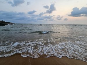 Beach scene at dusk, with gentle waves washing onto the sandy shore. The sky is filled with soft clouds, and the overall atmosphere is peaceful and serene. Captured from Kappad, Kozhikode, Kerala.

