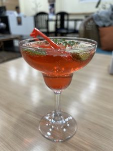A mocktail with mint, lemon and red coloring with carbonated water in a margarita glass.
