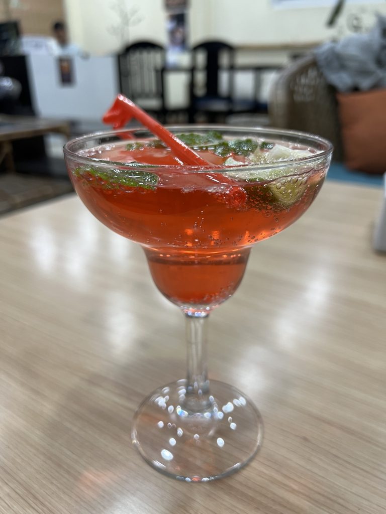 A mocktail with mint, lemon and red coloring with carbonated water in a margarita glass.
