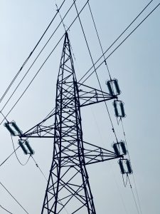 A tall metal electrical transmission tower with several power lines extending from it against a clear blue sky.