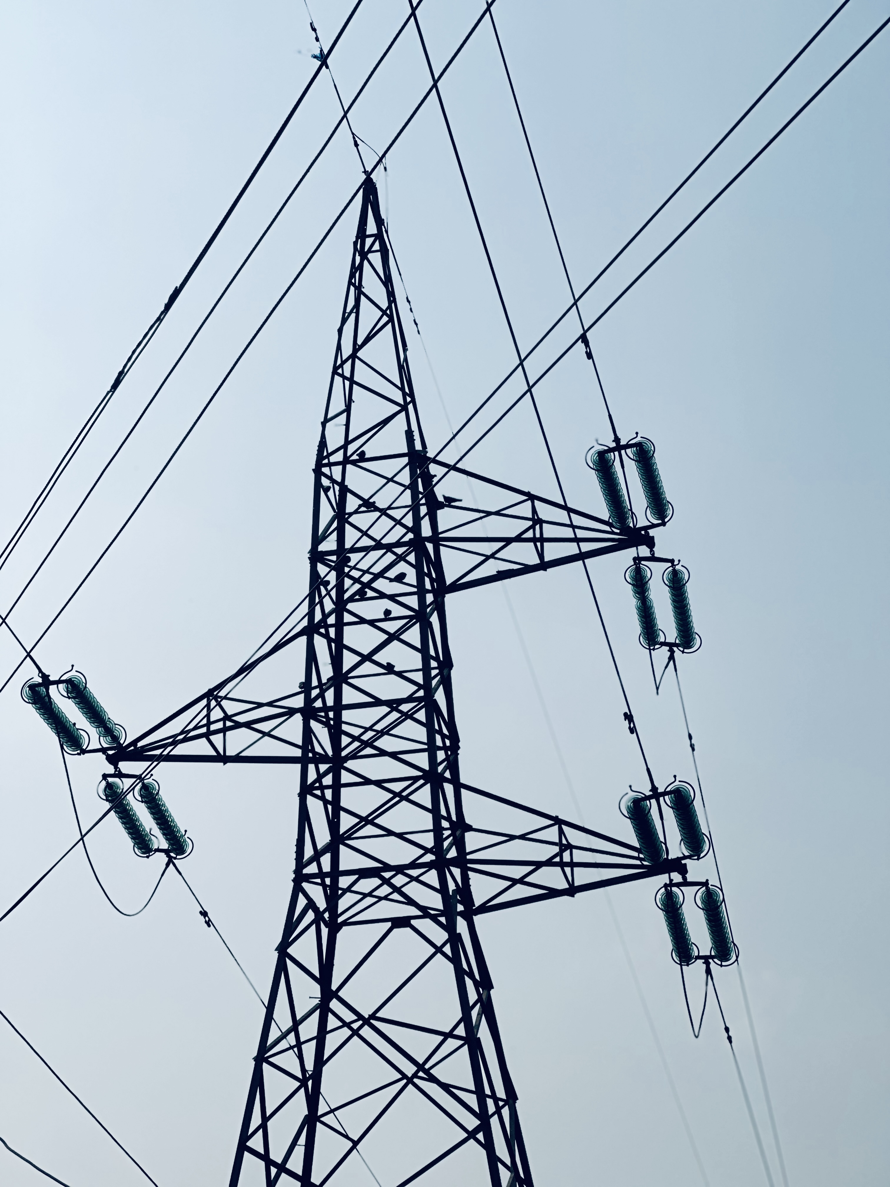 A tall metal electrical transmission tower with several power lines extending from it against a clear blue sky.