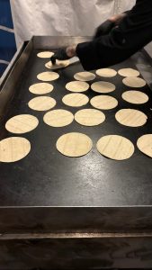 A griddle with tortilla's being warmed, a hand in the frame flipping one.