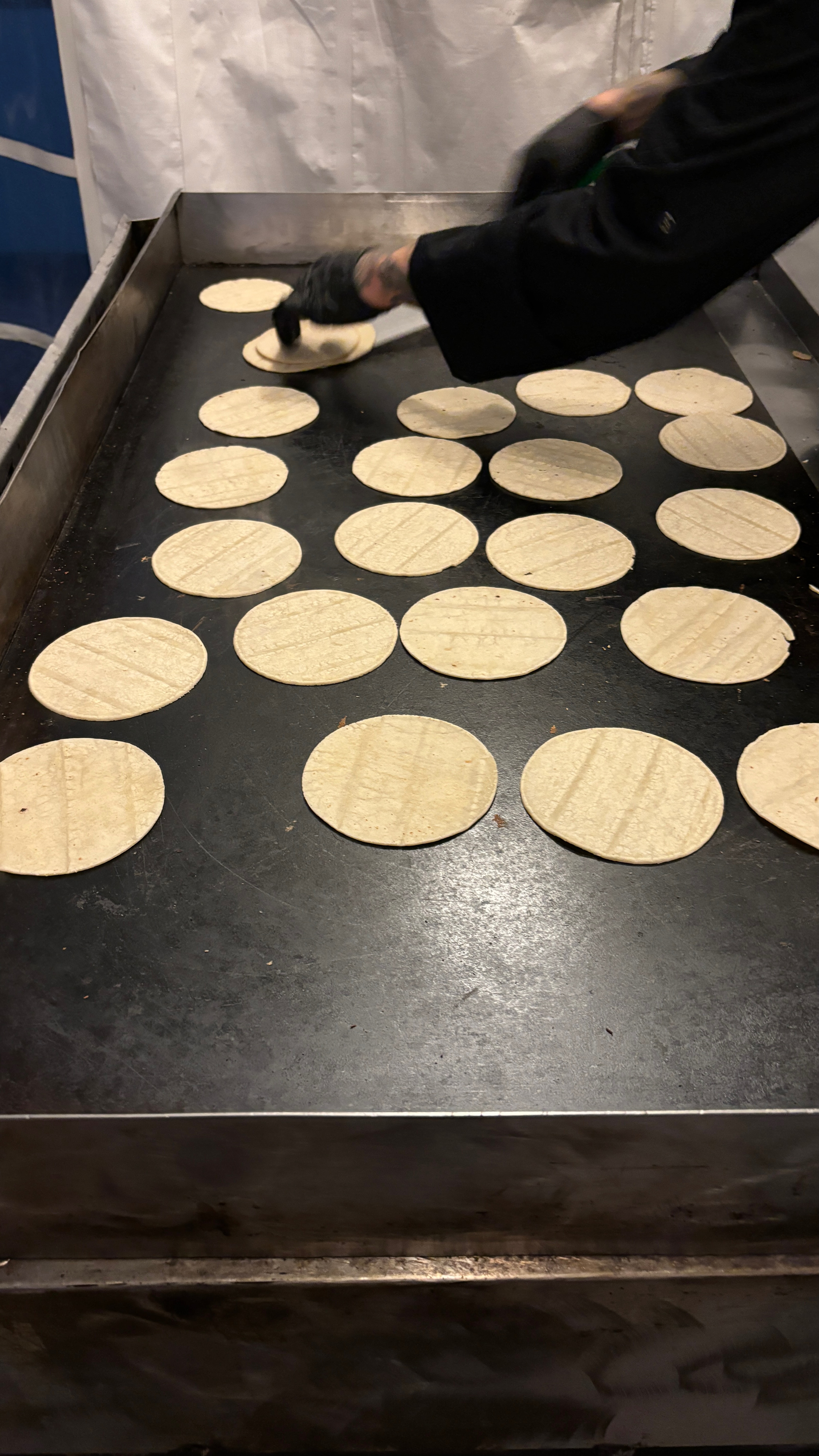 A griddle with tortilla's being warmed, a hand in the frame flipping one.