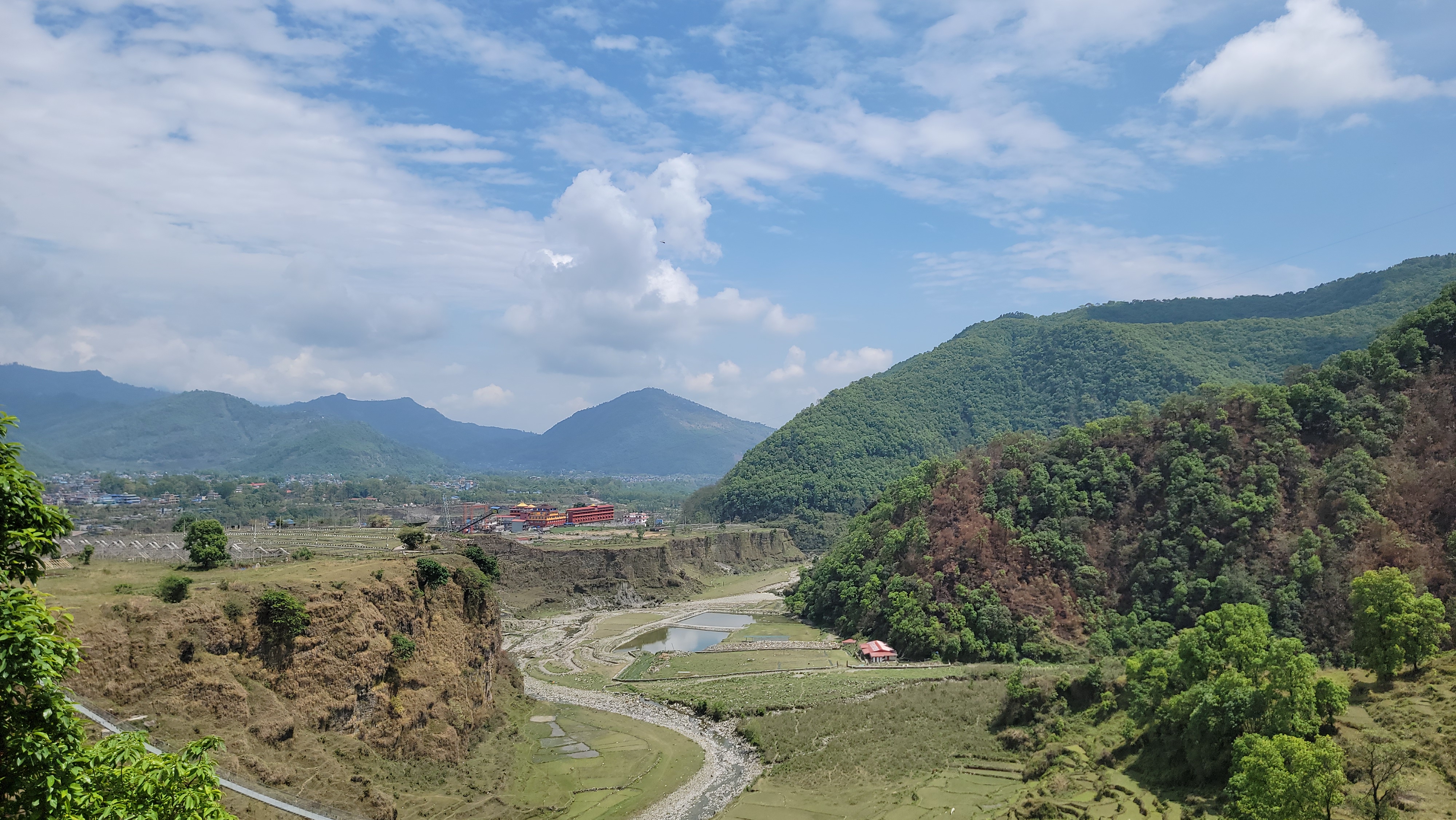 A panoramic view of a lush green landscape featuring rolling hills and mountains under a partly cloudy sky.