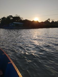 A serene view of a lake at sunset, with the sun low in the sky casting warm light over the water.