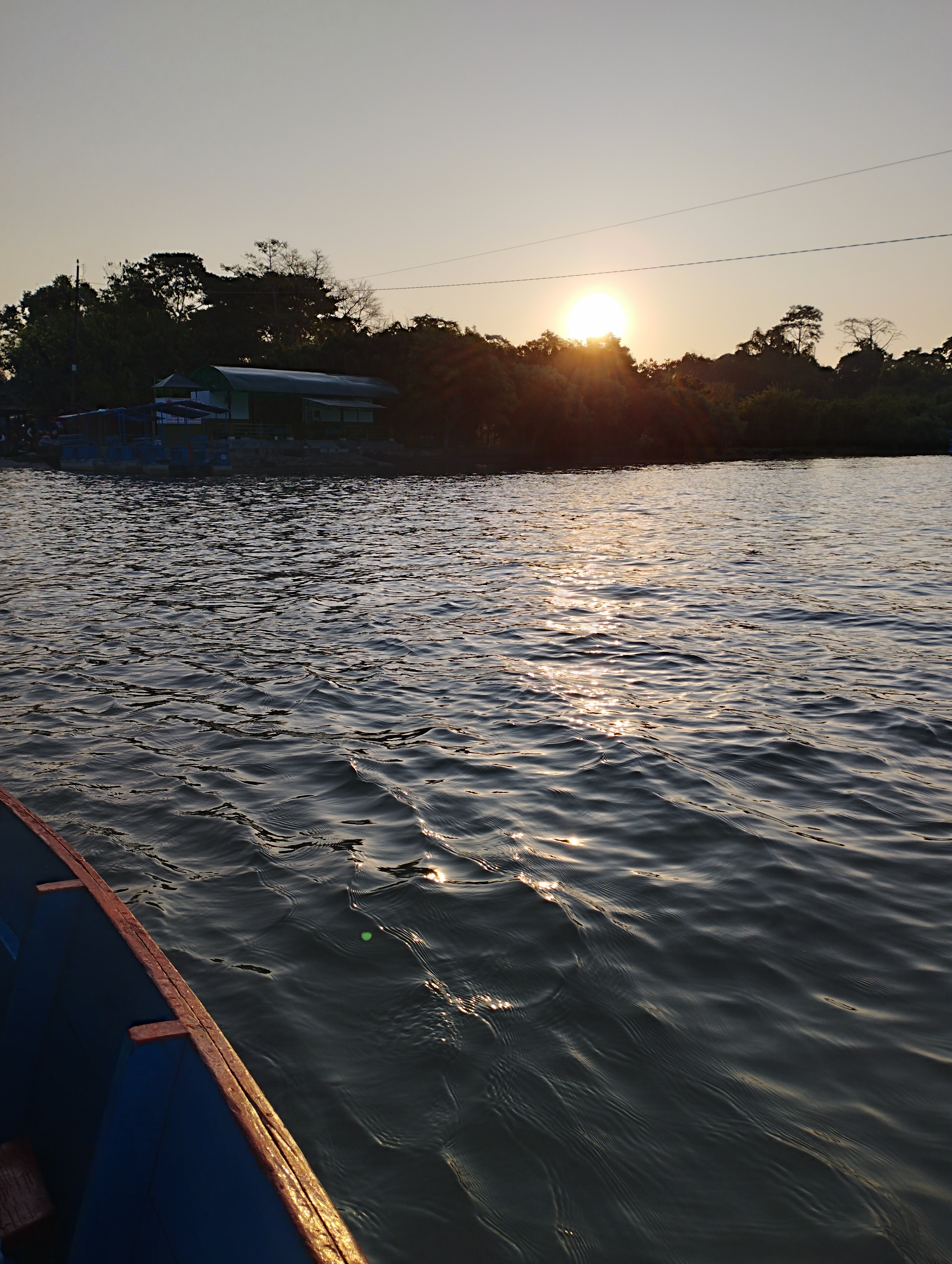 A serene view of a lake at sunset, with the sun low in the sky casting warm light over the water.