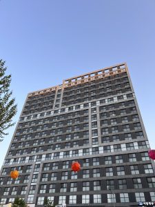 A tall, modern building with a dark exterior and large windows is shown against a clear blue sky. 