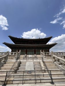 A grand traditional building with a tiered roof is seen against a blue sky dotted with fluffy white clouds.