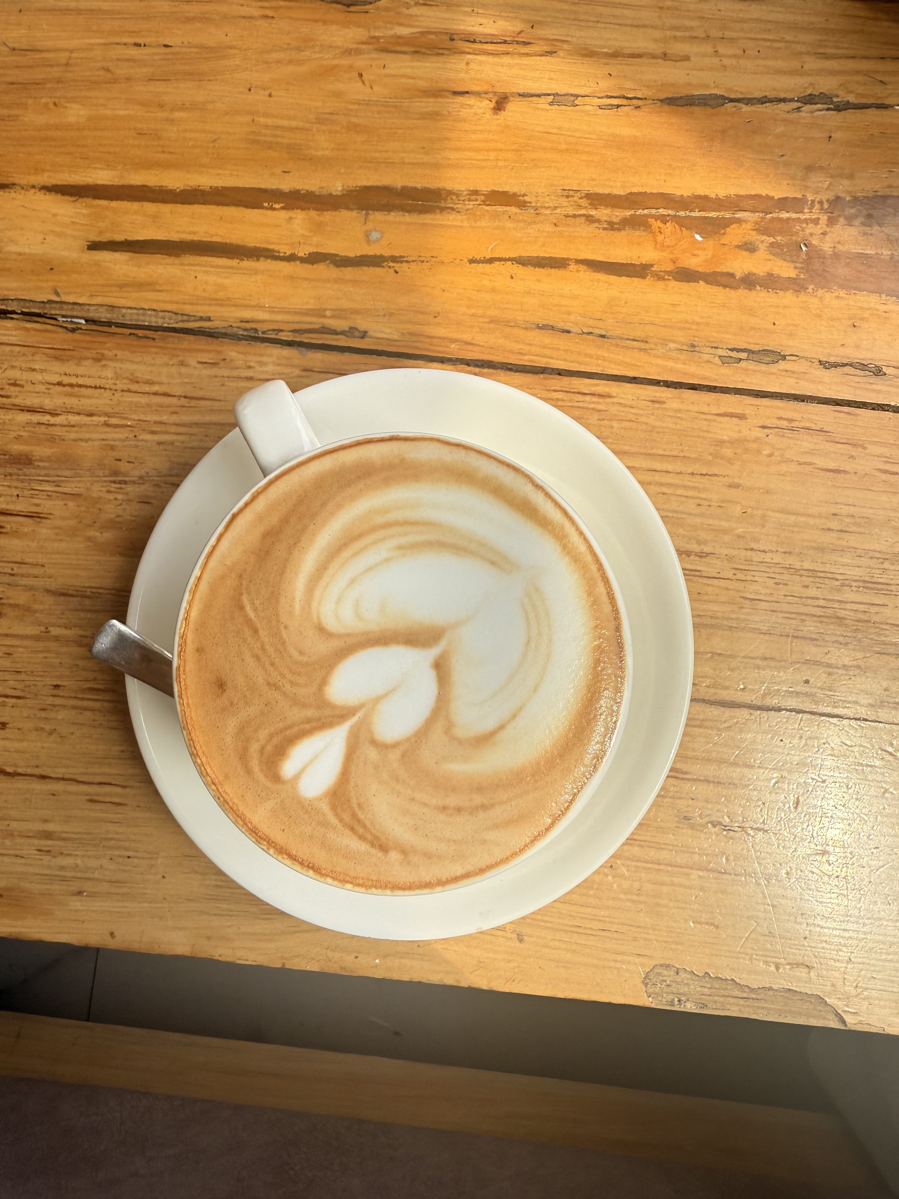 A cup of coffee with intricate latte art on top, placed on a saucer on a wooden table.