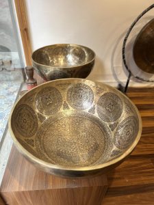 Two intricately engraved brass bowls are displayed, one placed inside the other, on a wooden surface