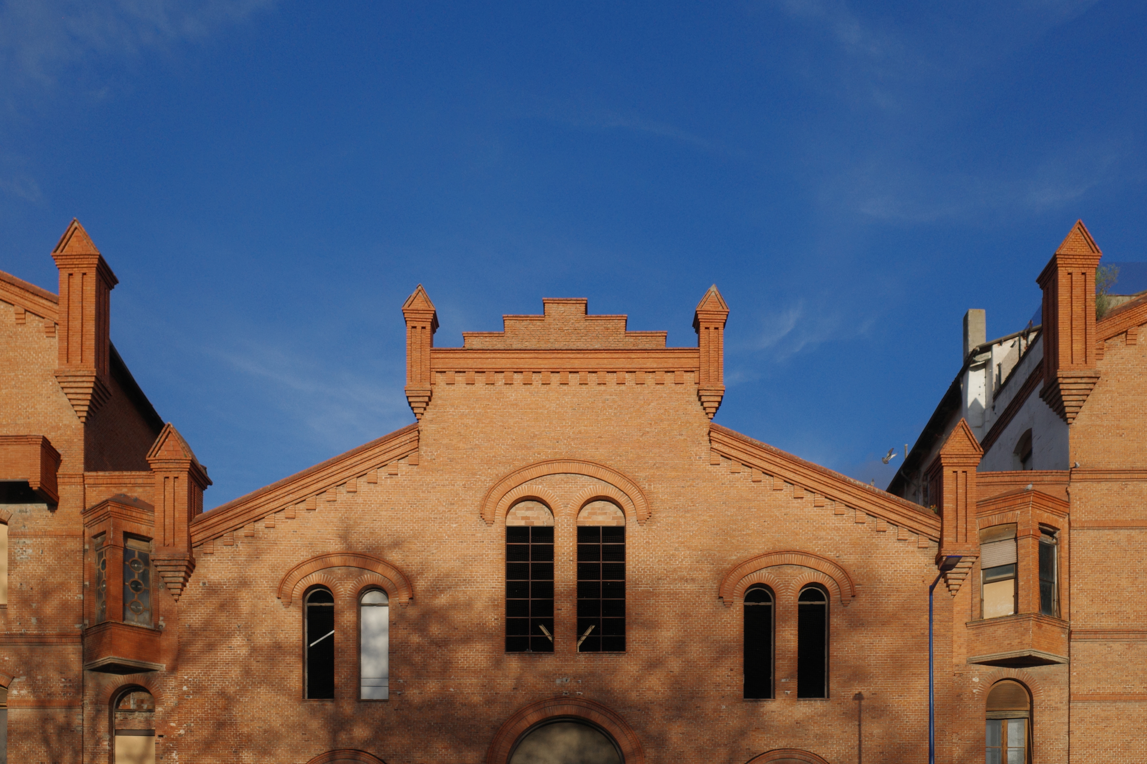 Red-brick building with a symmetrical facade featuring arched windows and ornate brickwork under a clear blue sky.