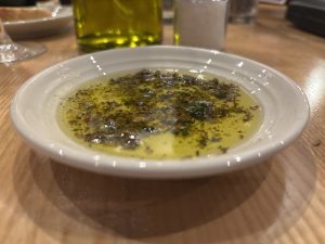 A small white plate filled with olive oil and herbs for dipping bread in.