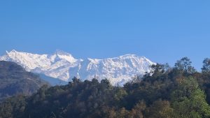 A scenic view of snow-capped mountains under a clear blue sky, with lush green hills in the foreground.