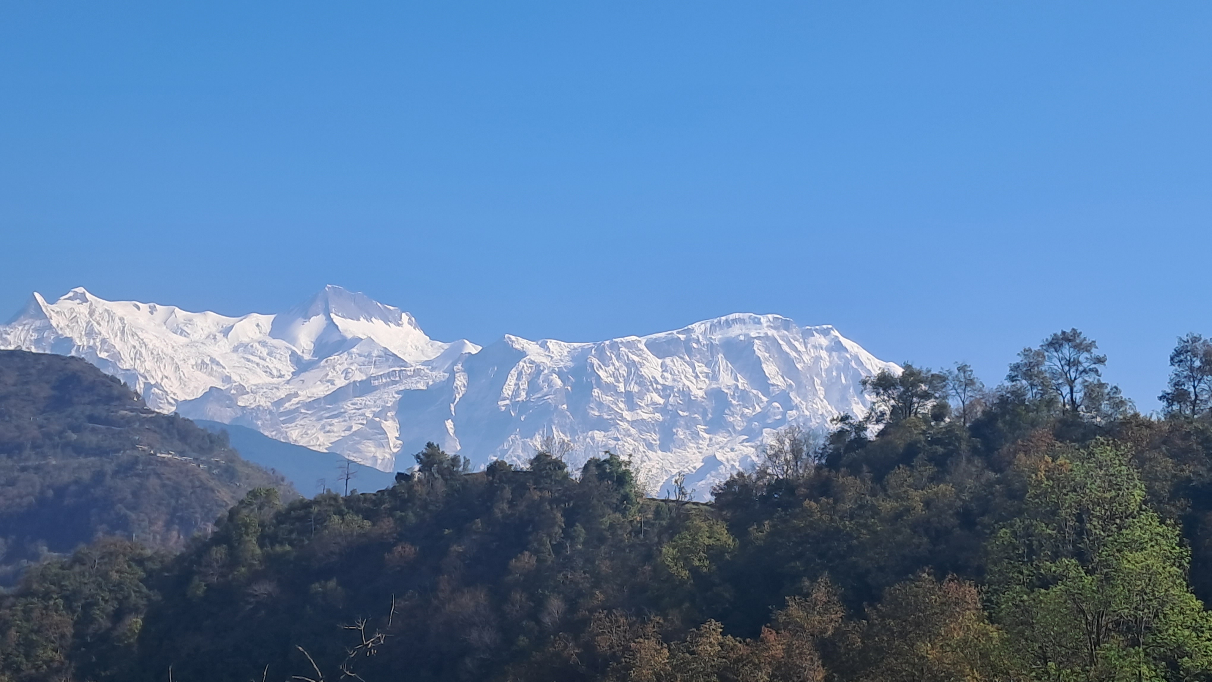 A scenic view of snow-capped mountains under a clear blue sky, with lush green hills in the foreground.