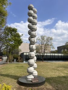 A tall sculpture consisting of stacked spherical forms made of stone, displaying a pattern of light and dark stripes