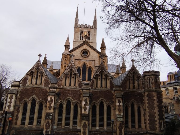 An ornate Gothic-style cathedral with multiple pointed arches and tall spires, featuring intricate stonework. The structure is surrounded by bare tree branches against an overcast sky.