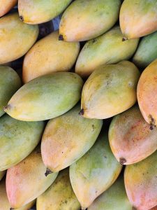 A close-up of a pile of mangoes, showcasing their vibrant colors ranging from green to yellow and orange, indicating different stages of ripeness. Spotted it at a market in Kozhikode, Kerala.