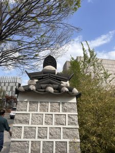 A decorative stone wall features a traditional tiled roof with a unique black ornament at the peak. 