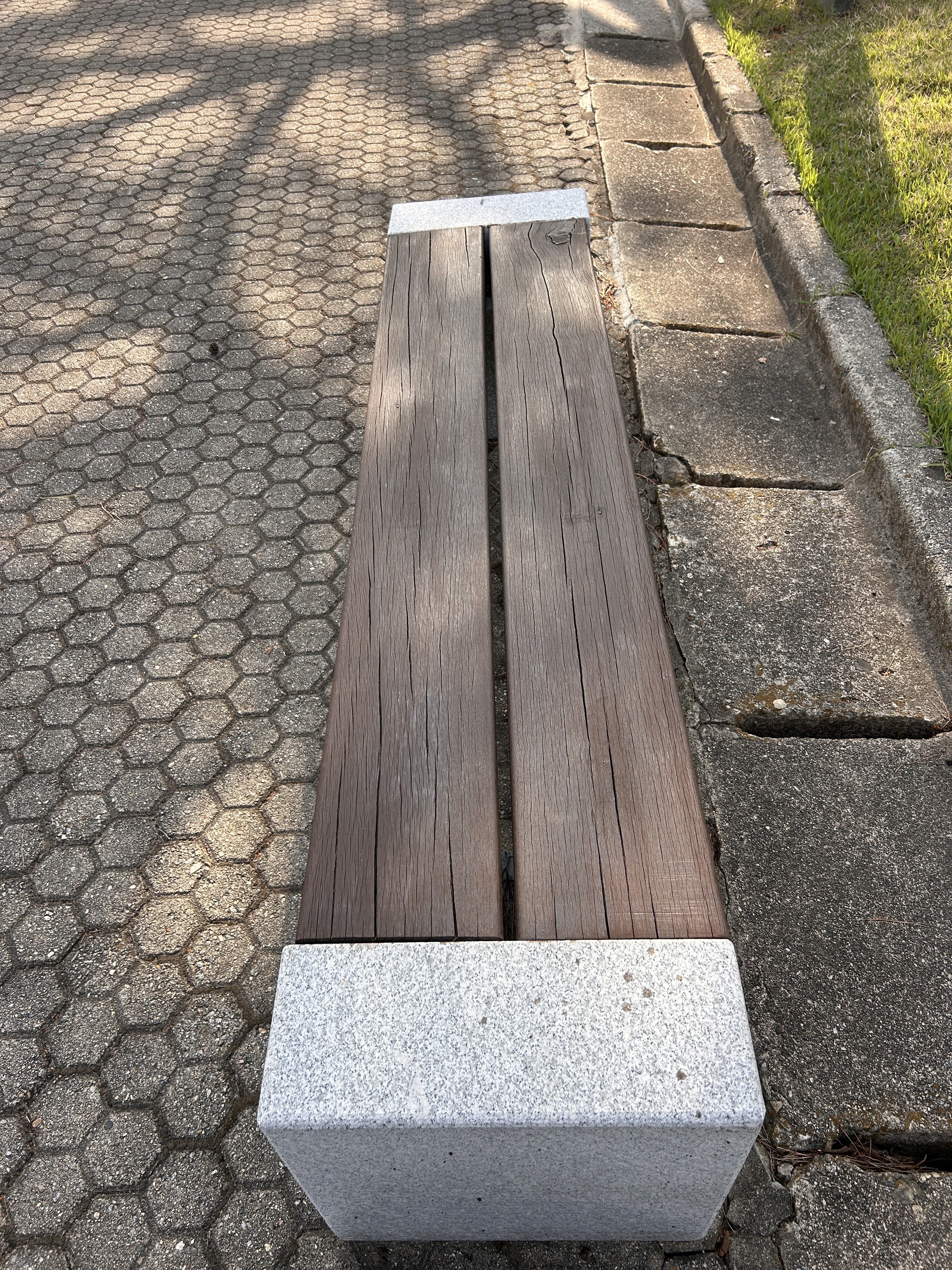 A simple wooden bench with two long, dark wooden planks as the seating surface, supported by light-colored stone end pieces.