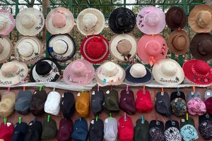A vibrant street-side collection of stylish hats and caps, showcasing a mix of sun hats with playful embroidery and colorful baseball caps. Perfect for sunny days and fashionable outings.
