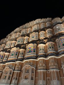 An ornate building facade with multiple small windows featuring colorful stained glass and intricate architectural details, illuminated against a dark night sky.