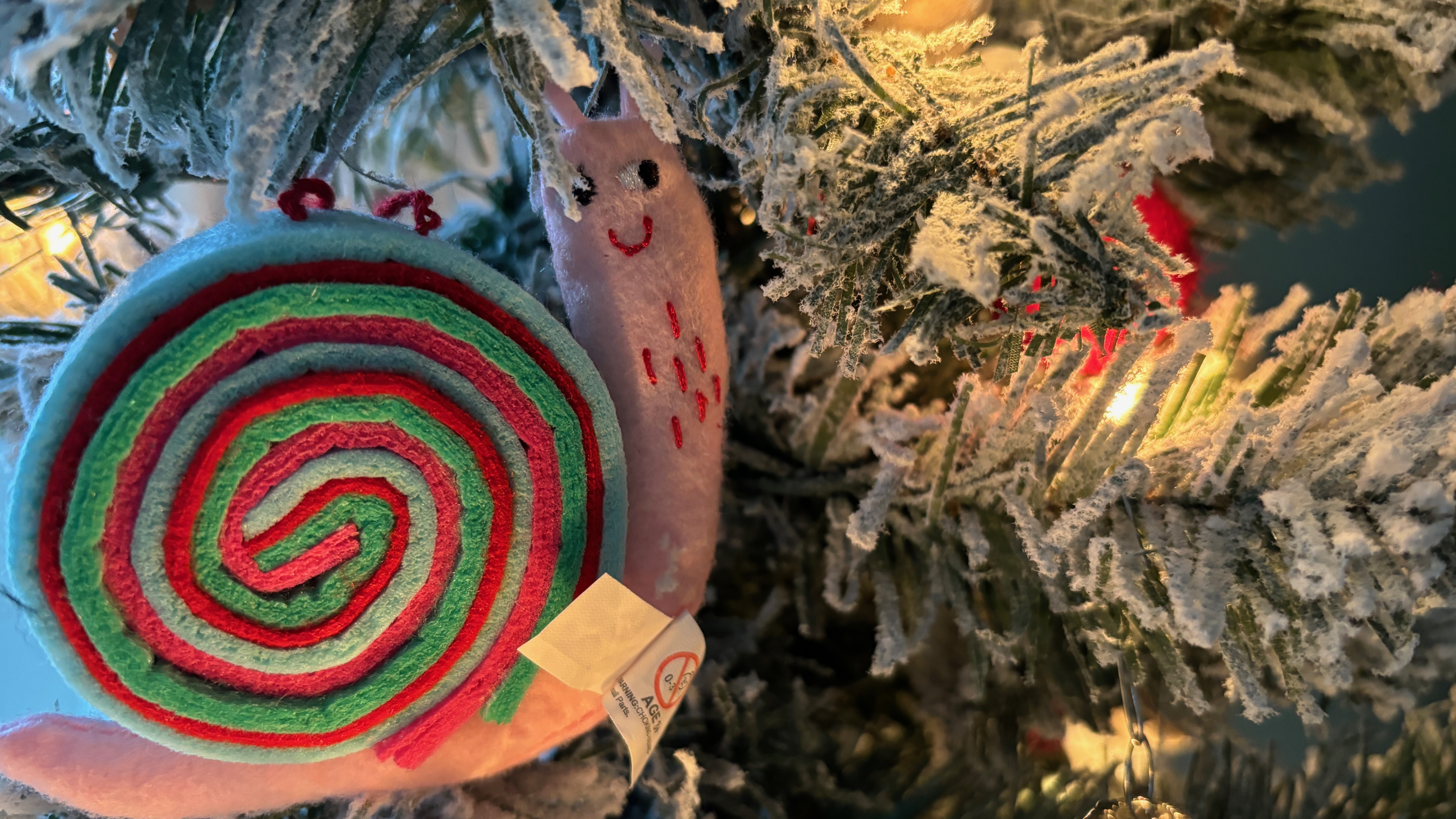 Closeup of a Christmas tree ornament shaped like a snail, whimsical colors.
