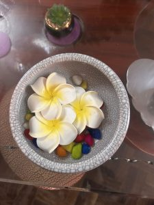 A decorative bowl containing artificial white and yellow flowers sits on a glass surface