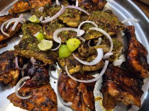 A platter of Al Faham chicken (Green Chili and Honey Chili flavors), garnished with sliced onions and lime wedges. The chicken pieces are arranged in a circular pattern, displaying a mix of golden-brown and slightly charred surfaces, indicative of the cooking process. It was captured in Kozhikode, Kerala.