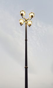 A tall street lamp with four illuminated lanterns arranged in a circular pattern against a cloudy sky.