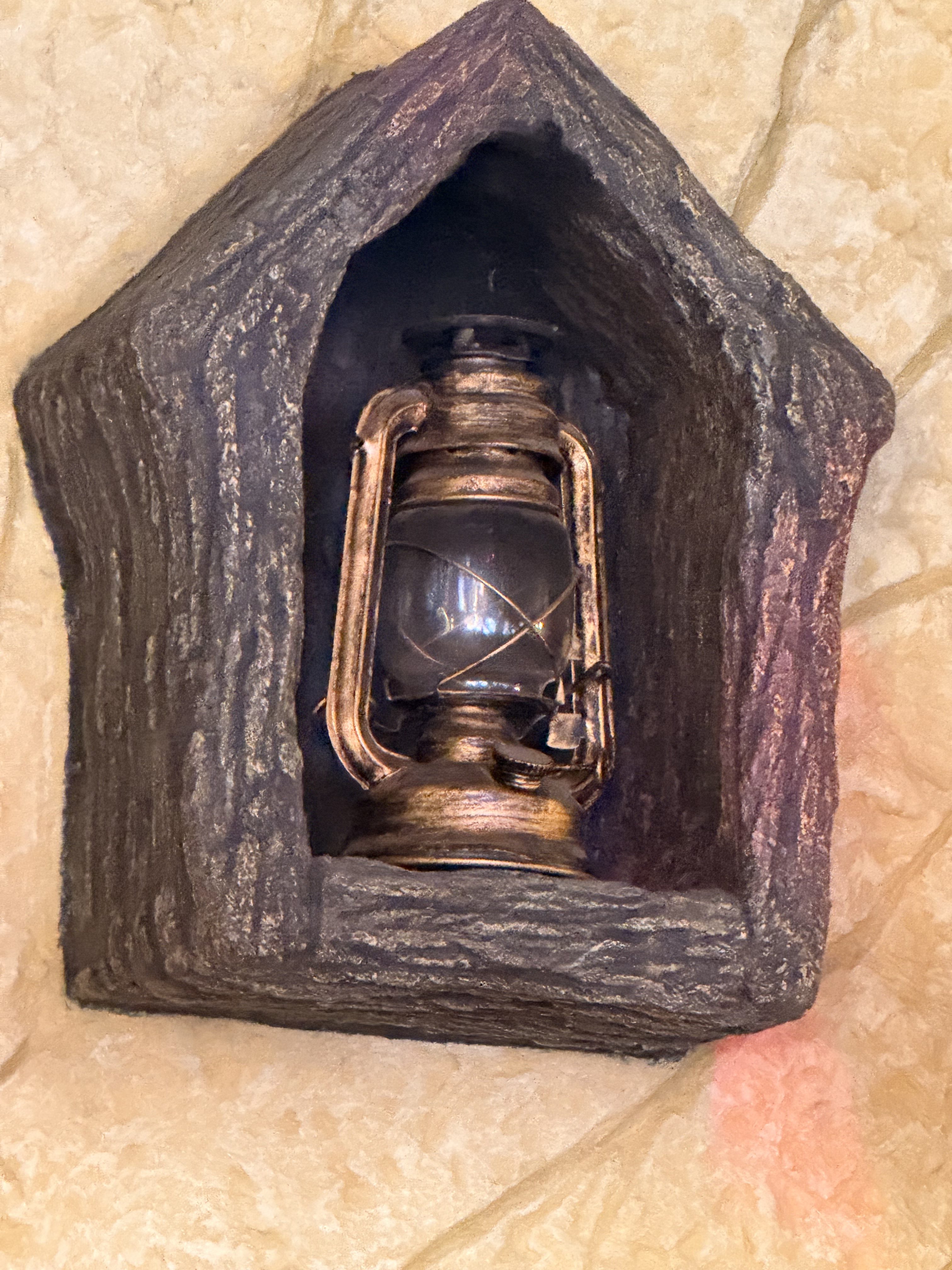 A vintage lantern enclosed in a rustic, wooden frame mounted on a textured wall.